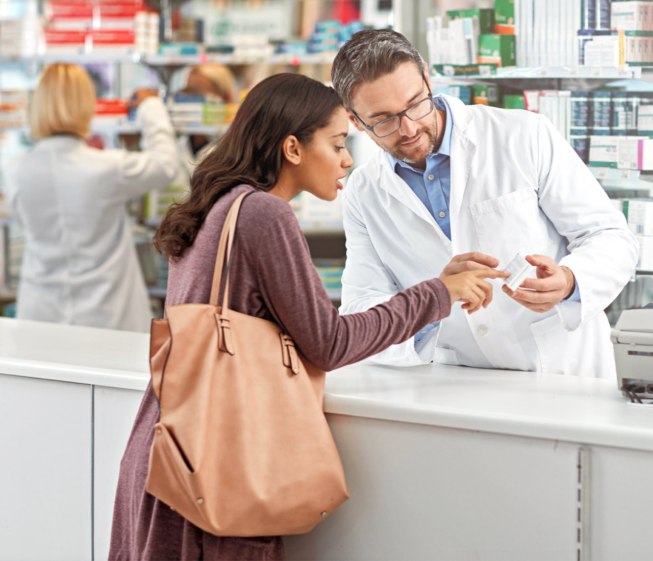 A woman talking to a pharmacist pointing to a medicine box.