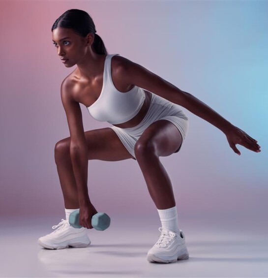A woman in workout attire squatting with a dumb bell