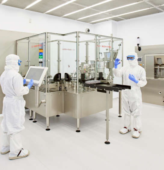 Two workers in white clean suits working on a machine.