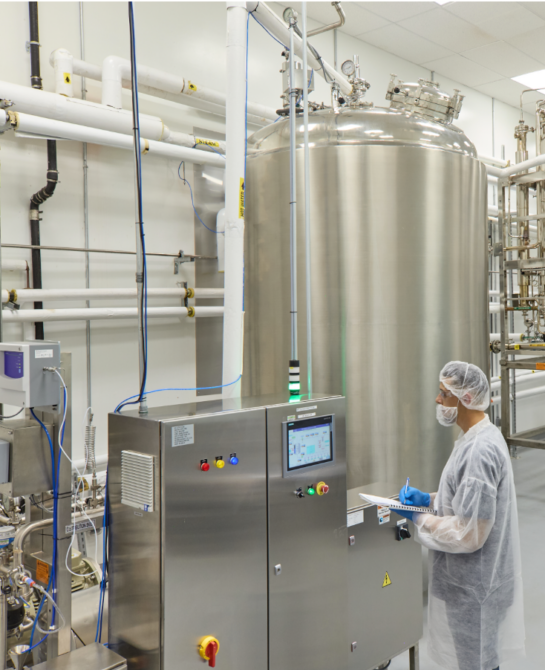 A worker in clean attire next to a machine.
