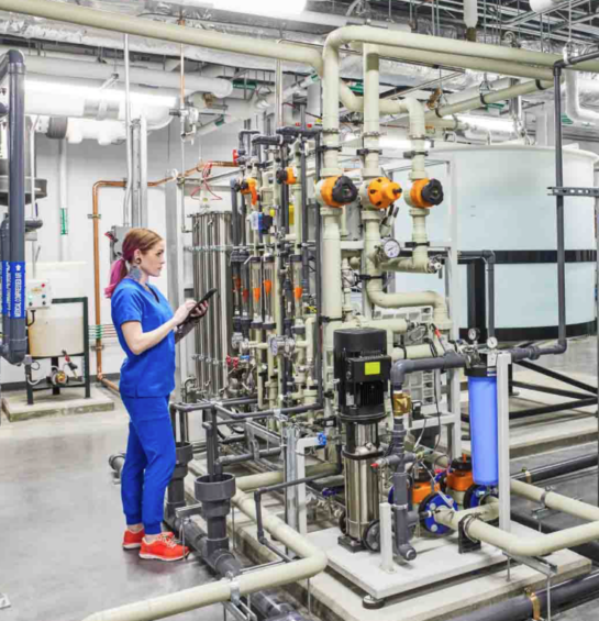 A woman in blue scrubs looking at a machine while on a tablet