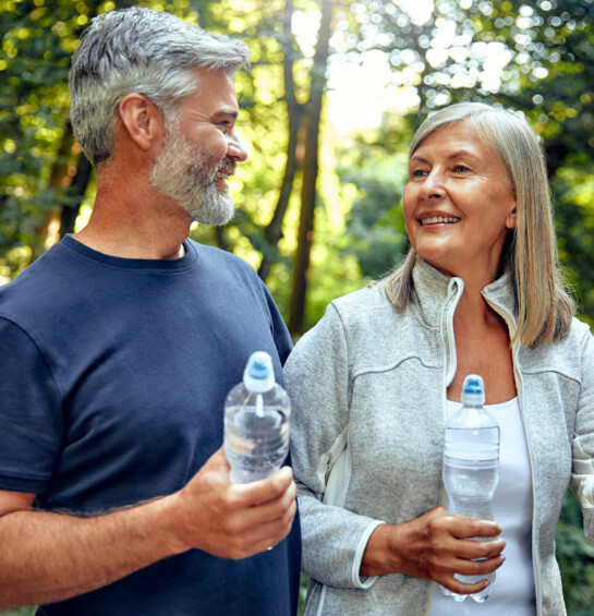 older couple hiking in woods holding water bottles